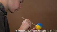 A child who fled the war from neighboring Ukraine paints an Easter egg in the colors of the Ukrainian flag during an event for Ukrainian refugee children on Maundy Thursday in a center for refugees in Bucharest, Romania, Thursday, April 21, 2022. Orthodox worshipers, which form the majority of Romanians, celebrate Easter Sunday, April 24. (AP Photo/Andreea Alexandru)