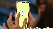 ILLUSTRATION - Ein Mädchen hält ihr Smartphone in den Händen, auf dem das Logo vom Instant-Messaging-Dienst Snapchat zu sehen ist. e Sorgen um wirtschaftliche Folgen des russischen Krieges in der Ukraine schlagen auf das Werbegeschäft der Foto-App Snapchat durch. (Zu dpa Sorgen über Ukraine-Krieg bremsen Snapchats Werbegeschäft) +++ dpa-Bildfunk +++
