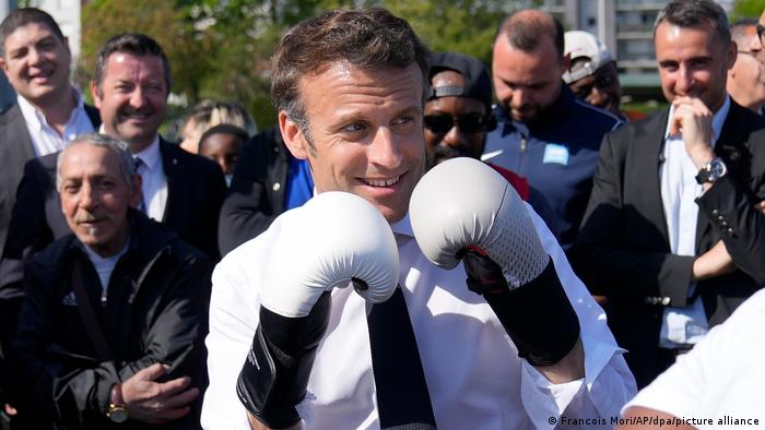 Emmanuel Macron holds up his hands in a the pose of a boxer, wearing white boxing gloves