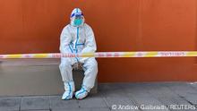 A worker in a protective suit sits near a police line outside a store, following the coronavirus disease (COVID-19) outbreak in Shanghai, China April 21, 2022. REUTERS/Andrew Galbraith
