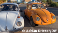 Two VW Beetles, one white and one orange, parked next to each other