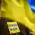 Mãos erguendo cartaz "Armamento pesado para a Ucrânia", em azul e amarelo