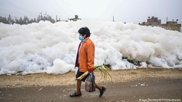 Una mujer camina junto a un muro de espuma que se formó en un río contaminado y que invadió el barrio de Los Puentes, en Mosquera, al oeste de Bogotá.