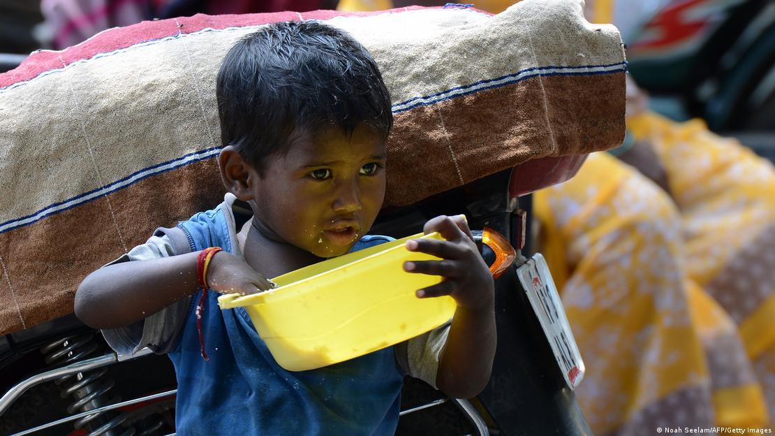 Criança come com as mãos, segurando uma bacia amarela