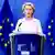 Ursula von der Leyen giving a speech in front of two EU flags