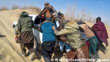In this picture taken on February 17, 2022, Afghan migrants push a pickup truck stuck in a desert road toward the Afghanistan-Iran border in Nimruz. - In Zaranj, a border town in southwestern Afghanistan, people smugglers say the flow of would-be exiles now reaches 5,000 to 6,000 a day -- four times more than before the Taliban's return to power in August. - TO GO WITH Afghanistan-Pakistan-Iran-migration by Romain FONSEGRIVES and Qubad WALI (Photo by Wakil KOHSAR / AFP) / TO GO WITH Afghanistan-Pakistan-Iran-migration by Romain FONSEGRIVES and Qubad WALI (Photo by WAKIL KOHSAR/AFP via Getty Images)