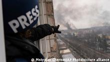 AP journalist Maloletka leaning out of a window, pointing at smoke rising in the distance after an airstrike 