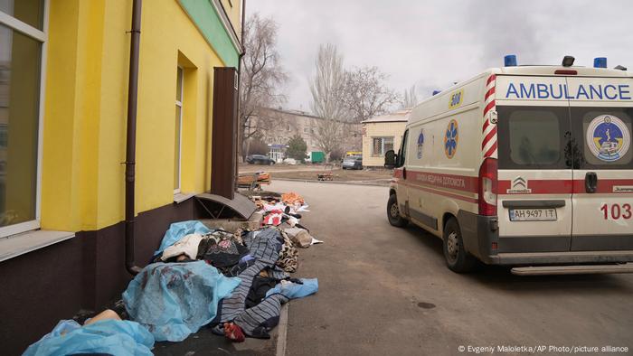 An ambulance passes the covered bodies of people killed by shelling