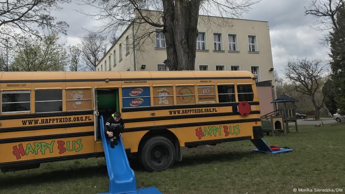 A child plays on a blue slide coming out of a yellow school bus