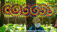 A vendor wearing a face mask sits near pinwheels for sale at a public park in Beijing, Saturday, April 30, 2022, the first day of the Labor Day holiday period in China. (AP Photo/Mark Schiefelbein)