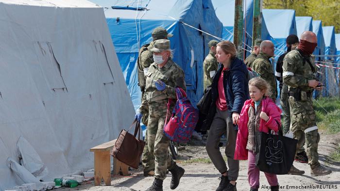 Civilians who left the area near Azovstal steel plant in Mariupol walk accompanied by a service member of pro-Russian troops at a temporary accommodation center 