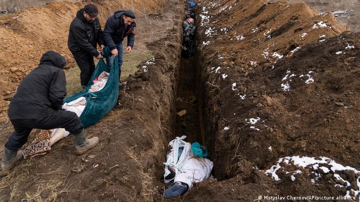 Three men throwing a body wraped in sheets into a trench on the outskirts of Mariupol, Ukraine, Wednesday, March 9, 2022