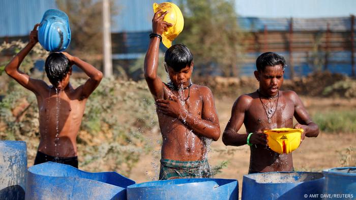 Workers use their helmets to pour water to cool themselves off near a construction site on a hot summer day on the outskirts of Ahmedabad, India