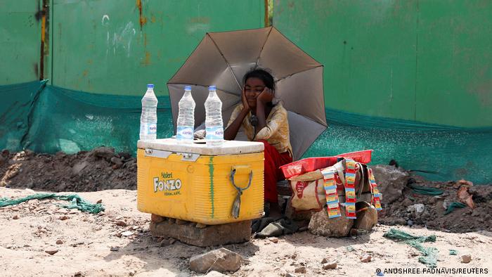 A girl selling water uses an umbrella to protect herself from the sun in New Delhi, India