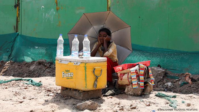 A girl selling water uses an umbrella to protect herself from the sun in New Delhi, India