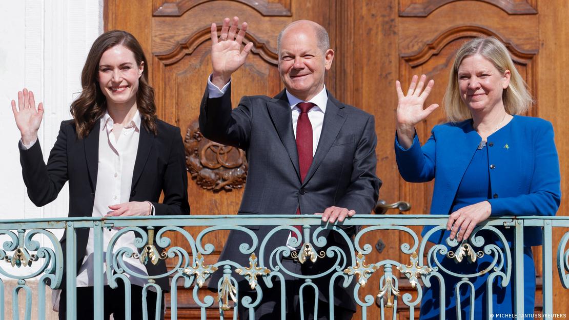 A primeira-ministra da Finlândia, Sanna Marin, o chanceler federal alemão, Olaf Scholz, e a primeira-ministra da Suécia, Magdalena Andersson. Eles aparecem acenando com a mão direita em uma sacada.