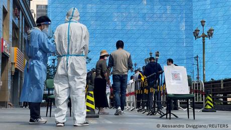 Workers in protective suits stand by a line of citizens waiting to be tested in Beijing