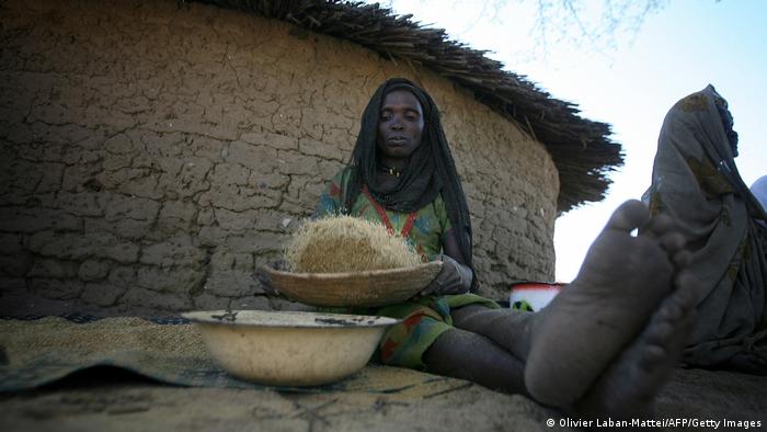 Women sitting in front of hut with big bowls of with millets