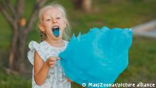 Little blond girl eating cotton candy and shows blue color tongue in the park || Modellfreigabe vorhanden