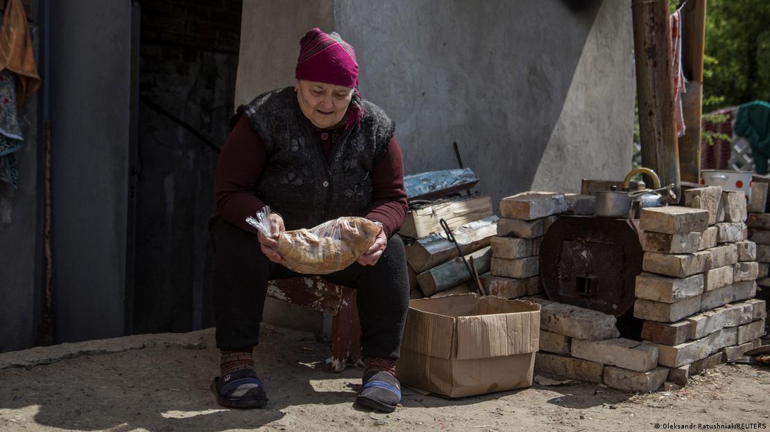 Mulher sentada em frente a uma casa pobre, segura um pão