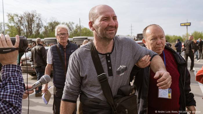 A man supports another man as he walks through a parking lot after arriving on the convoy