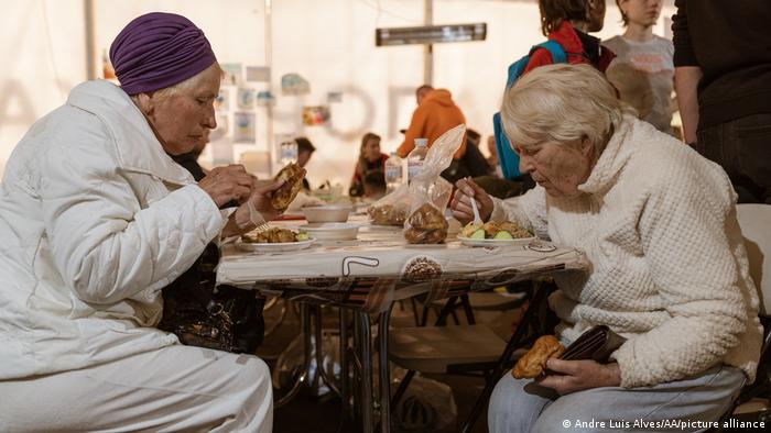 Two women who have been evacuated from Mariupol eat a meal while sitting at a table