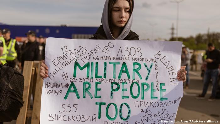 A young person holds up a sign that reads Military are people too
