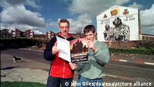 ARCHIV - 11.04.1998, Norirland, Belfast: Zwei Männer lesen in dem am Vortag unterzeichneten Friedensabkommen vor einer Hauswand mit einem Mural und dem Spruch Prepared for Peace Ready for War. (zu 20 Jahre Karfreitagsabkommen: Der unvollendete Frieden vom 09.04.2018) Foto: John_Giles/epa/dpa +++ dpa-Bildfunk +++