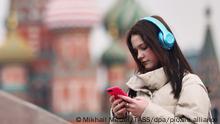 DIESES FOTO WIRD VON DER RUSSISCHEN STAATSAGENTUR TASS ZUR VERFÜGUNG GESTELLT. [MOSCOW, RUSSIA - MARCH 25, 2022: A girl in headphones looks at her mobile phone near St Basil's Cathedral in early spring. Alexander Shcherbak/TASS]