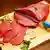Um pedaço de carne é cortado em bifes e tiras, sobre uma tábua, junto a um pedaço de limão e um dente de alho.