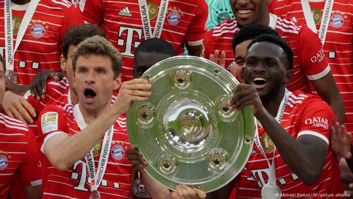 Thomas Müller and Tanguy Nianzou cheer with the championship trophy in hand