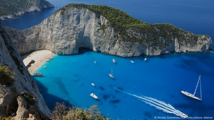 Das blaue Meer mit einigen Schiffen darauf. Drumherum sind Felsen und Felsvorsprünge zu sehen.