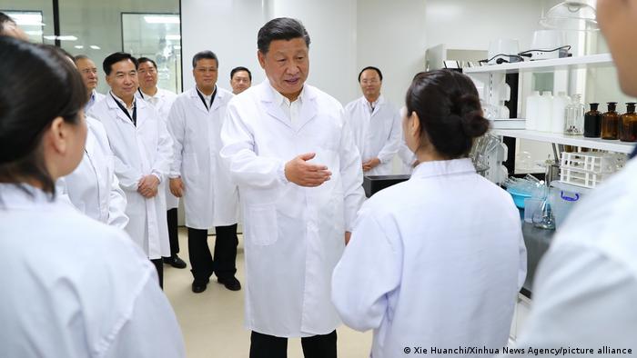 Chinese President Xi Jinping speaks with employees at the Traditional Chinese Medicine Science and Technology Industrial Park, all wearing white lab coats