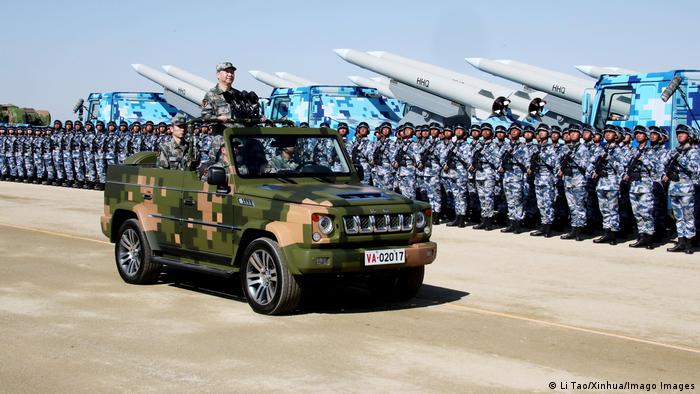 Military parade in 2017 with a camouflaged jeep rolling past a line of soldiers and rockets 