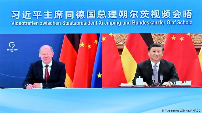 Bundeskanzler Olaf Scholz (l.) und Xi Jinping während eines Videogesprächs; im Hintergrund die schwarz-rot-goldene deutsche Fahne und die mit gelben Sternen versehene chinesische Fahne in Rot. 