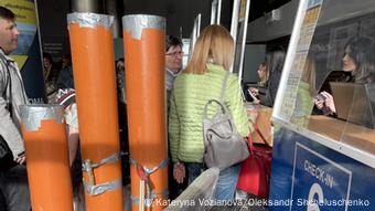 Άνθρωποι σε έναν πάγκο check-in, τρεις ψηλοί πορτοκαλί σωλήνες αποχέτευσης στέκονται δίπλα τους. Άνθρωποι σε έναν πάγκο check-in, τρεις ψηλοί πορτοκαλί σωλήνες αποχέτευσης στέκονται δίπλα τους.