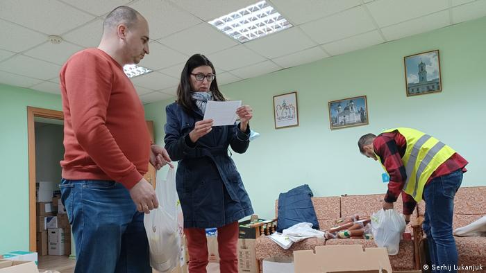 Drei Helfer sortieren Spenden in einem Raum mit einem Sofa und zahlreichen Pappkartons im Flur