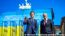 Bundeskanzler Olaf Scholz (r, SPD) und Frankreichs Präsident Emmanuel Macron stehen nach einem Treffen vor dem Brandenburger Tor. Aus Anlass des Europatages ist das Brandenburger Tor in den ukrainischen Nationalfarben beleuchtet.