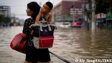 Eine Frau trägt ein Kind durch die Überschwemmungen in Zhengzhou, China 