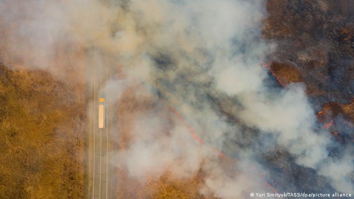 An aerial view of a wildfire in the Razdolnaya River valley while a truck drives through smoke