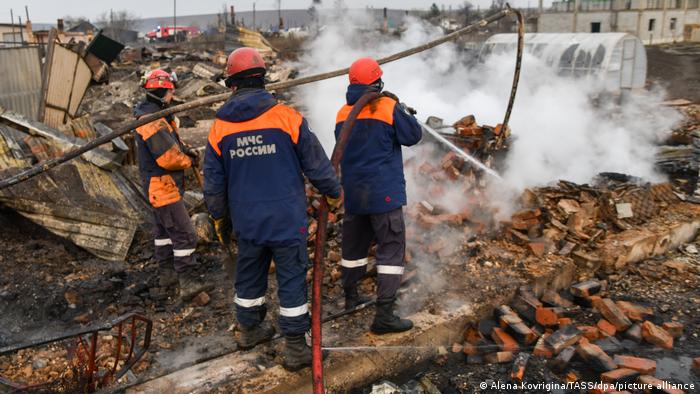 Employees of the Russian Emergencies Ministry fight a fire in a residential area in the town of Uyar in Russia's Krasnoyarsk Territory, standing amid ruins