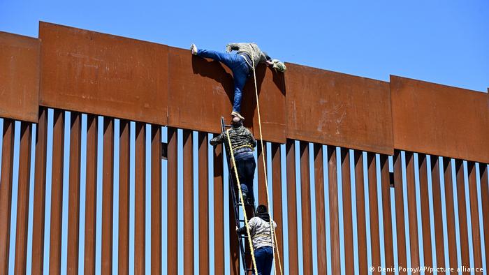 Personas migrantes utilizan una escalera para pasar la valla fronteriza entre México y Estados Unidos en Tecate.