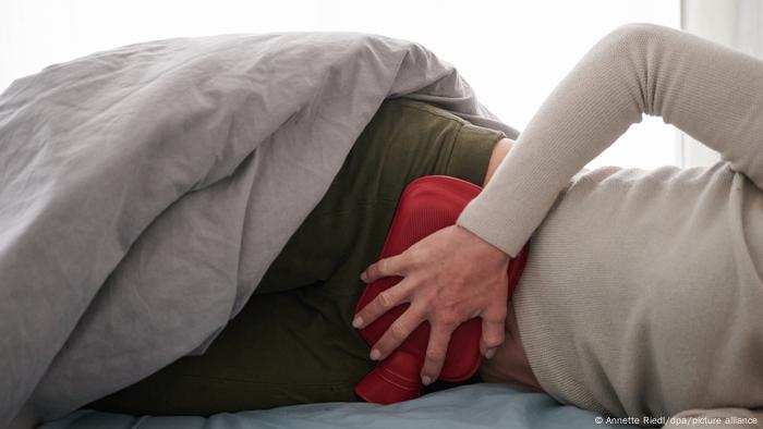 A woman holds a hot water bottle to her lower abdomen while lying in bed