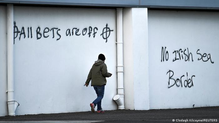 A man walks past a wall with loyalist graffiti reading 'All bets are off' and 'No Irish sea border'