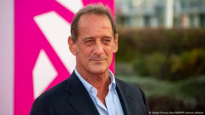 Cannes Filmfestival: Vincent Lindon steht in hellblauem Hemd und dunkelblauem Jackett vor einem pinken Hintergrund