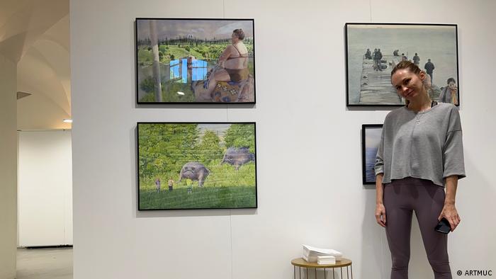 A woman standing in front of four framed paintings in an art gallery.