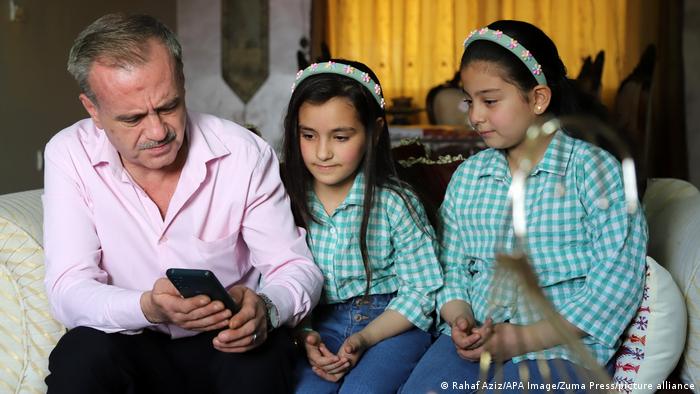 father and two daughters look at phone