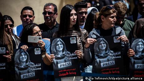 Mourners hold signs as they attend a memorial service in the West Bank city of Ramallah for journalist Shireen Abu Akleh 