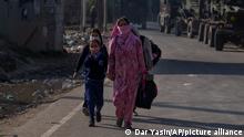 Kashmiri women along with children walk past parked vehicles of the Indian army