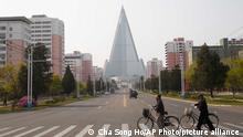 People wearing face masks cross a road in front of the Ryugyong Hotel in Pyongyang, North Korea Tuesday, April 28, 2020. (AP Photo/Cha Song Ho)